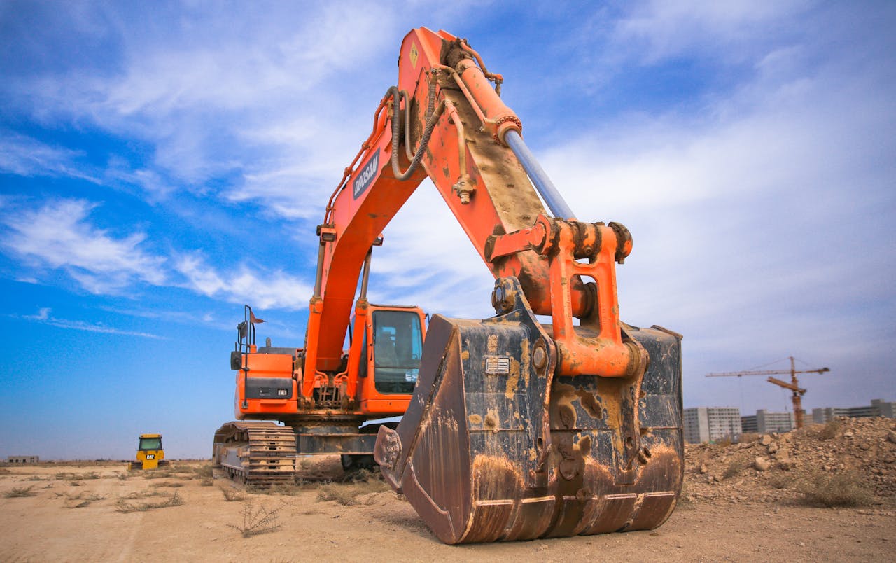 services-bg A large orange excavator working on a construction site under a blue sky.