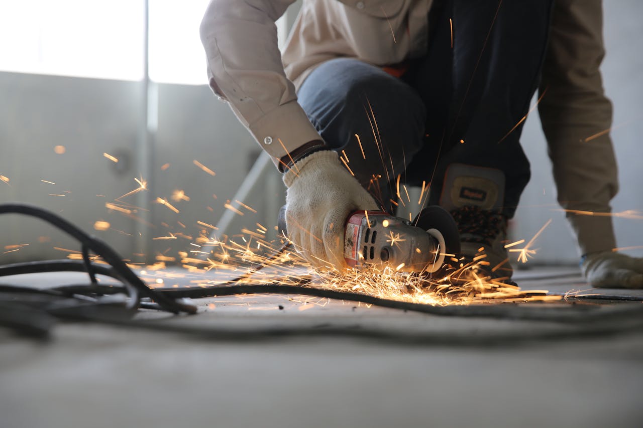 services-05 A skilled industrial worker uses a grinder creating a burst of sparks indoors.