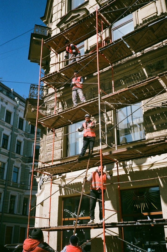 who-we-are Construction workers on scaffolding renovating a building facade on a sunny day.